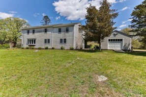 A two-story house with a garage, surrounded by a grassy yard. - Private Pickleball Court, Walk to Hen Cove (Bourne)