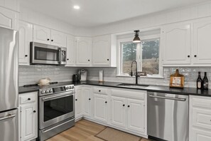 A modern kitchen with white cabinetry, stainless steel appliances, and a window with a view.