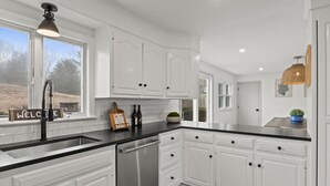 Cocina con armarios blancos, encimera negra y lavavajillas de acero inoxidable.