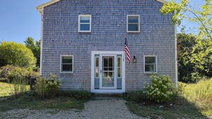 A two-story house with a front porch, a door with glass panels, and an American flag. - Private Pickleball Court, Walk to Hen Cove (Bourne)