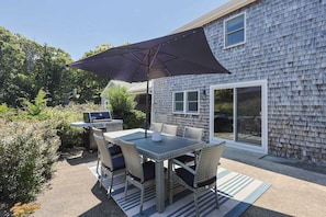 An outdoor patio with a table and chairs, a grill, and a large umbrella. - Private Pickleball Court, Walk to Hen Cove (Bourne)