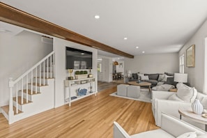 Un vaste espace de vie comprenant un escalier en bois, un ensemble de canapés et un coin repas.