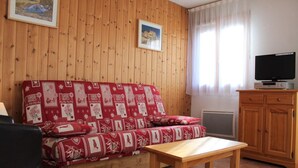 Un salon chaleureux avec un mur lambrissé en bois, un canapé rouge à motifs, une table en bois et un téléviseur posé sur un meuble en bois.
