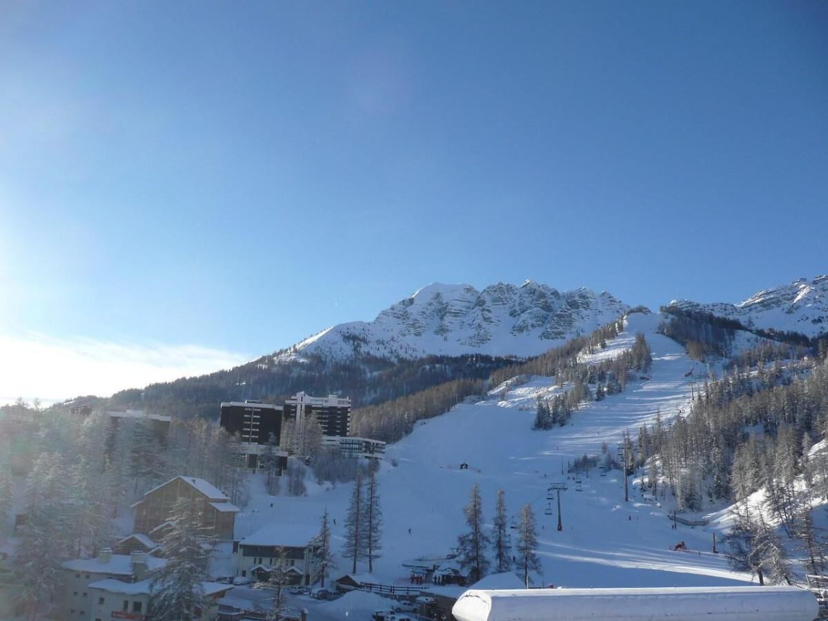 Une montagne enneigée avec une piste de ski, des bâtiments et des arbres.