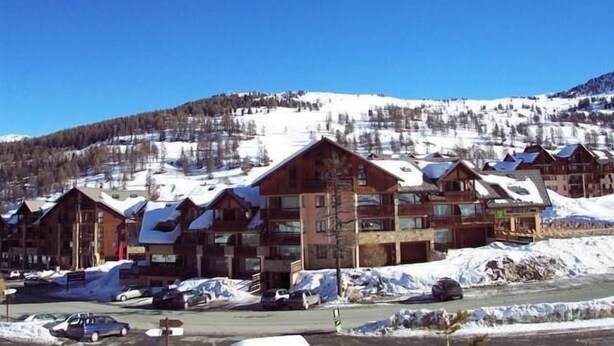 Une station de ski avec des bâtiments en bois, un parking et une montagne enneigée en toile de fond.