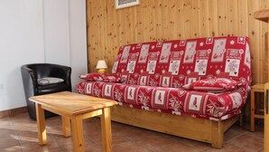 Une pièce aux murs lambrés, avec un canapé rouge à motifs, un fauteuil en cuir noir et une table en bois.