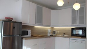 Une cuisine moderne avec des meubles blancs, un réfrigérateur en acier inoxydable, un four à micro-ondes blanc, une machine à café et un grille-pain.
