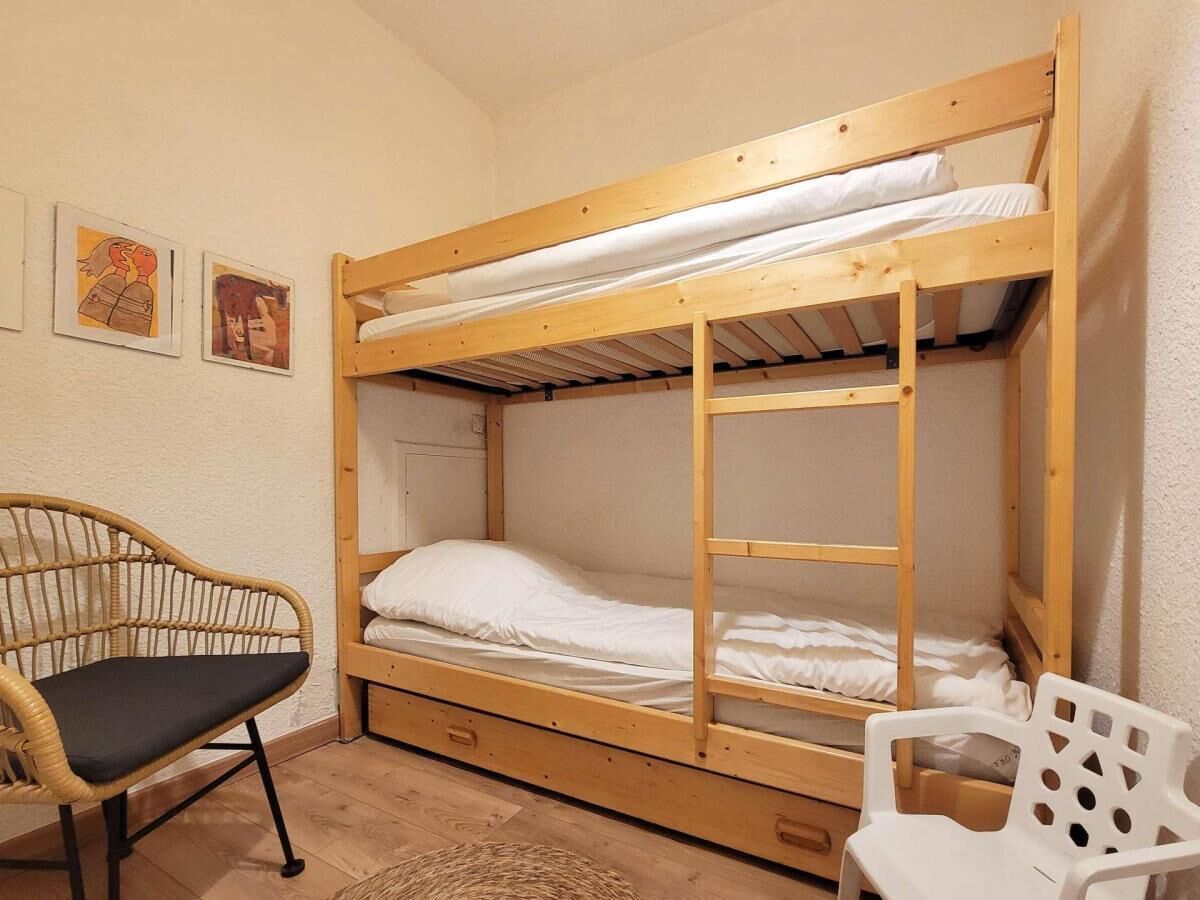 A bunk bed with a wooden frame, a single bed below, and a chair with a cushion.