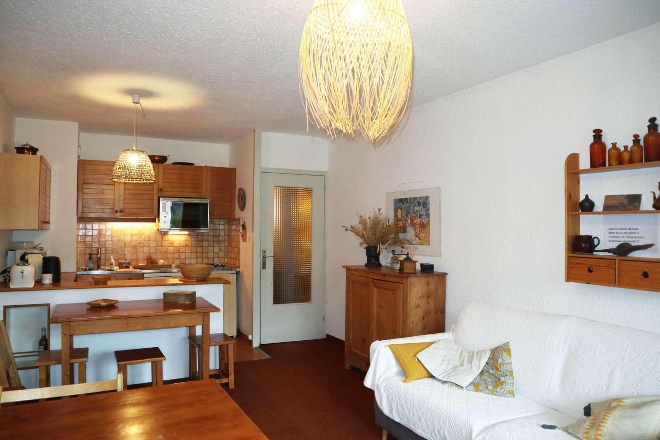 A compact living space with a kitchenette, a dining area, and a seating area with a sofa and cushions.