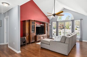 A spacious living room with a high ceiling, a large window, and a built-in entertainment unit.