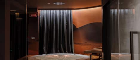 A modern spa room with a wooden floor, a hot tub, and a glass partition.