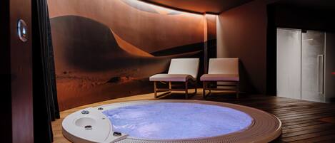 A modern spa room with a hot tub, wooden flooring, and two lounge chairs.