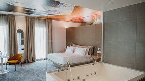 A modern hotel room with a large bed, a separate bathroom with a bathtub, a dining area with a table and chairs, and a large window with curtains. - Biancodonda Greenblu Hotel & SPA (Gallipoli)