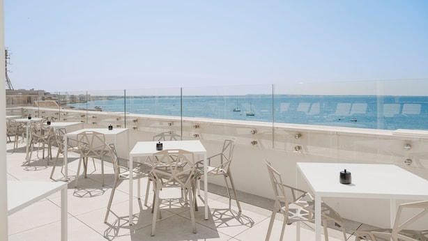 A terrace with white tables and chairs, a clear view of the sea, and a distant shoreline. - Biancodonda Greenblu Hotel & SPA (Gallipoli)