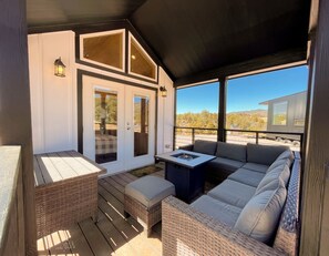 A covered outdoor seating area with a built-in fire pit, cushioned seating, and a view of the surrounding landscape.