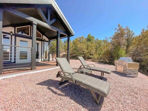 A covered outdoor seating area with two lounge chairs and a barbecue grill. - The Cabin (Cañon City)