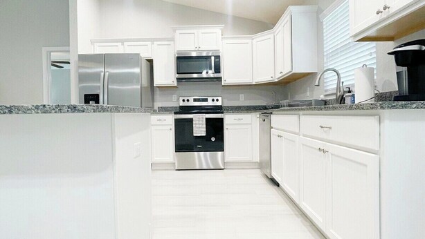 A modern kitchen with white cabinetry, stainless steel appliances, and a granite countertop. - Comfy and Cozy 4 bedroom home with garage (Ocala)