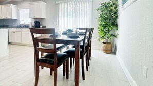A dining area with a wooden table and chairs, a potted plant, and a window with blinds. - Comfy and Cozy 4 bedroom home with garage (Ocala)