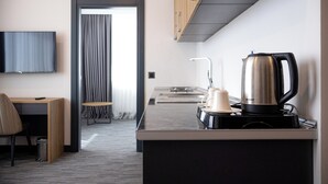 A modern hotel room with a flat-screen TV, a coffee maker, a kettle, and a small seating area with a chair and a table. - HOME PLUS HOTEL (Istanbul)