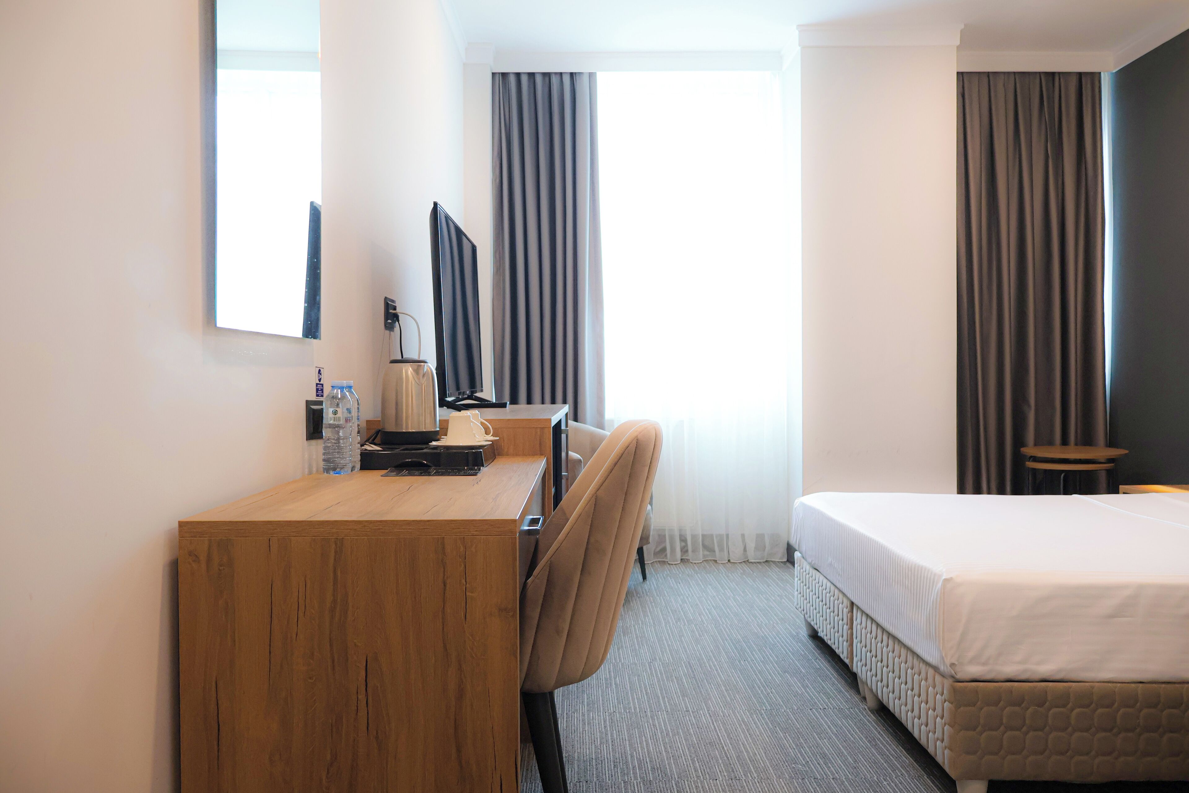 Habitación de hotel con un escritorio de madera, una silla, una cama, un televisor y una ventana con cortinas.