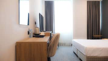 Habitación de hotel con un escritorio de madera, una silla, una cama, un televisor y una ventana con cortinas.