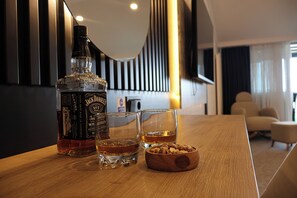 A bottle of Jack Daniel's whiskey, two glasses, and a bowl of nuts on a wooden table in a modern room with a piano in the background.