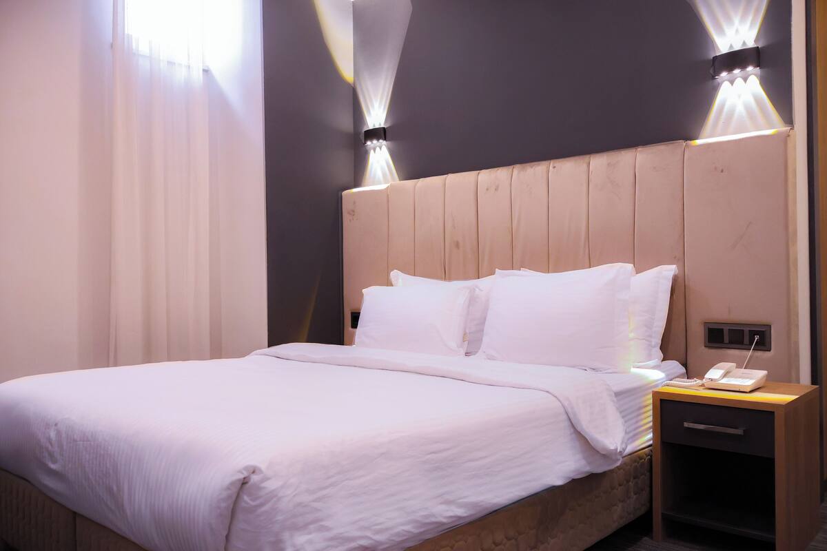 A neatly made bed with white linens, a wooden headboard, and a bedside table with a phone and a lamp.