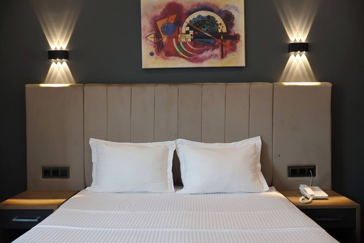A hotel room with a large bed, two bedside tables, a wall-mounted artwork, and two wall-mounted lamps.