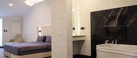 Ein modernes Schlafzimmer mit einem großen Bett, einer Sitzecke und einem Badezimmer mit Badewanne und Marmorwand.