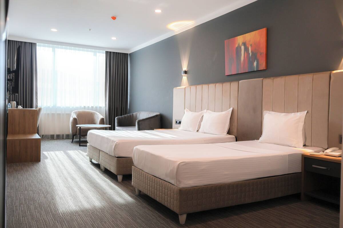 A hotel room with two beds, a desk, a chair, and a large window with curtains.