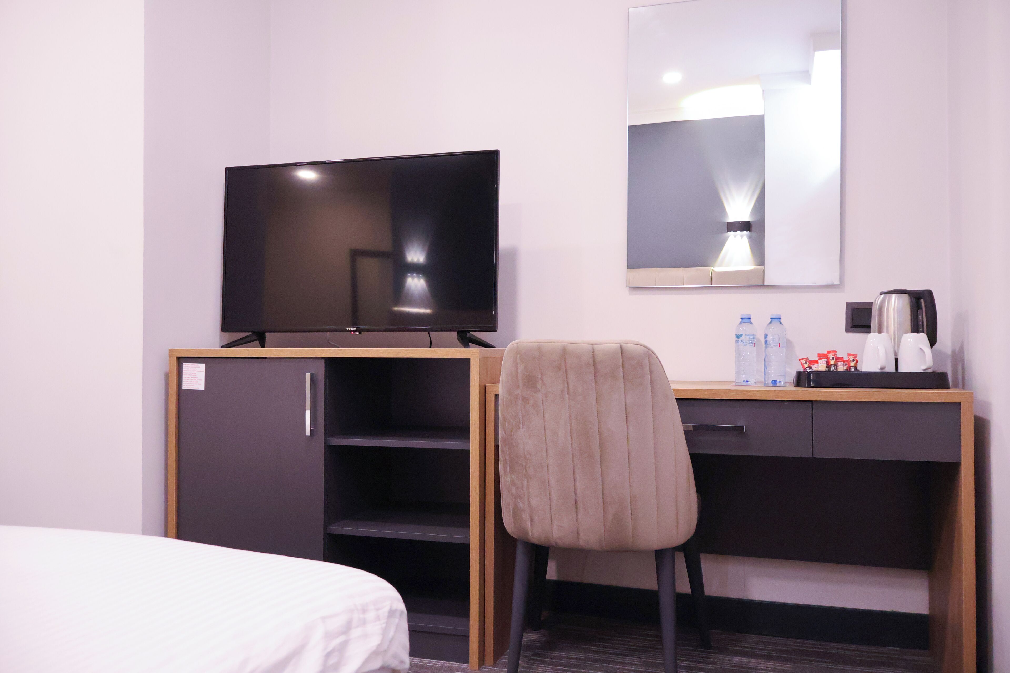 Ein Hotelzimmer mit einem Bett, einem Schreibtisch mit Fernseher, einem Sessel, einem Spiegel und einem kleinen Schrank.