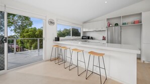 A modern kitchen with a large island, bar stools, and a view of the outdoors. - Seaworthy Sanctuary • Stylish Coastal Escape (Jan Juc)