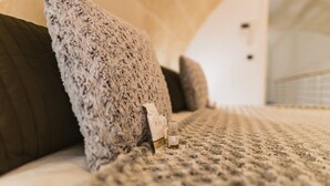 A bed with a textured blanket and pillows, a bottle of lotion, and a small bottle of essential oil on the bed. - [Sassi-Suite]- Aura - Matera (Milano)