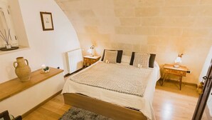 A cozy bedroom with a bed, bedside tables, a nightstand, a small shelf, and a rustic wall. - [Sassi-Suite]- Aura - Matera (Milano)