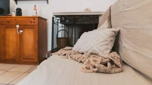 A bed with a beige blanket and a white pillow, a wooden cabinet, and a fireplace in the background. - Intrulloves- Complex of Trulli Storici Pugliesi (Milano)