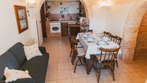 A cozy dining area with a table set for four, a sofa, and a kitchen in the background. - Intrulloves- Complex of Trulli Storici Pugliesi (Milano)
