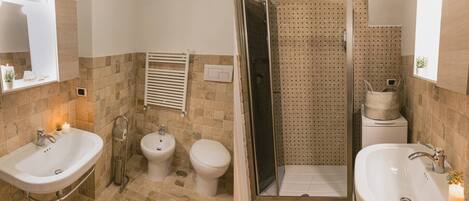 A bathroom with two sinks, a bidet, a toilet, and a shower area.