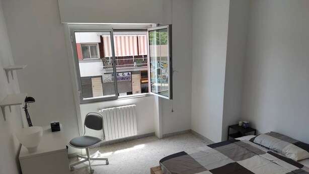 Un dormitorio con cama, escritorio, silla y ventana con vistas al exterior.