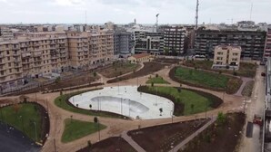 Una amplia plaza abierta con una fuente central, rodeada de áreas verdes y edificios residenciales.