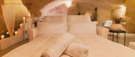 A cozy, dimly lit room with a large bed, pillows, and a small table with candles.