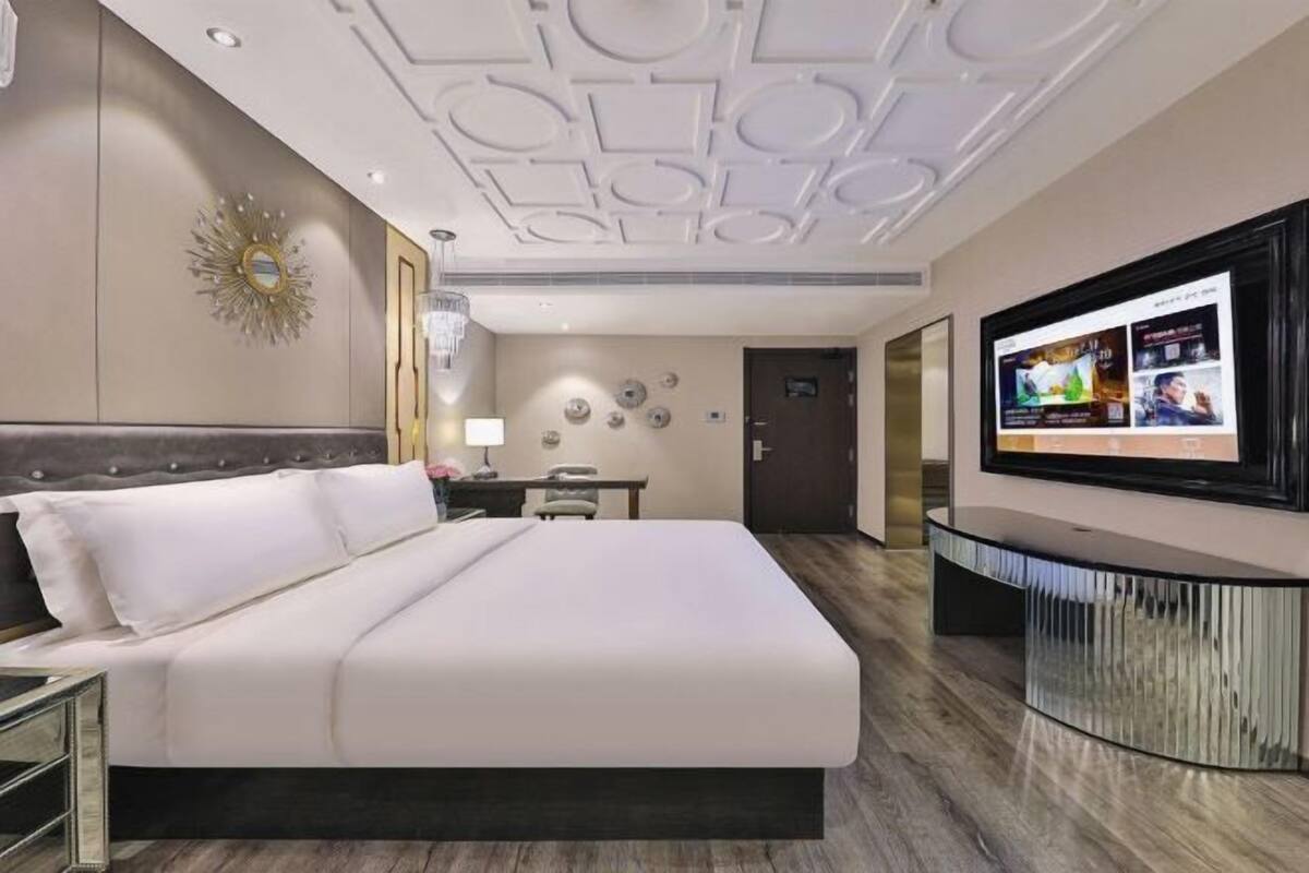 A hotel room with a large bed, a TV, a desk, and a mirror.