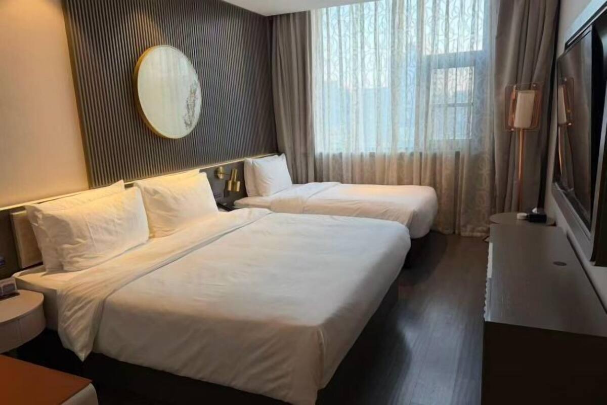 A hotel room with two beds, a large mirror, a TV, and a window with curtains.