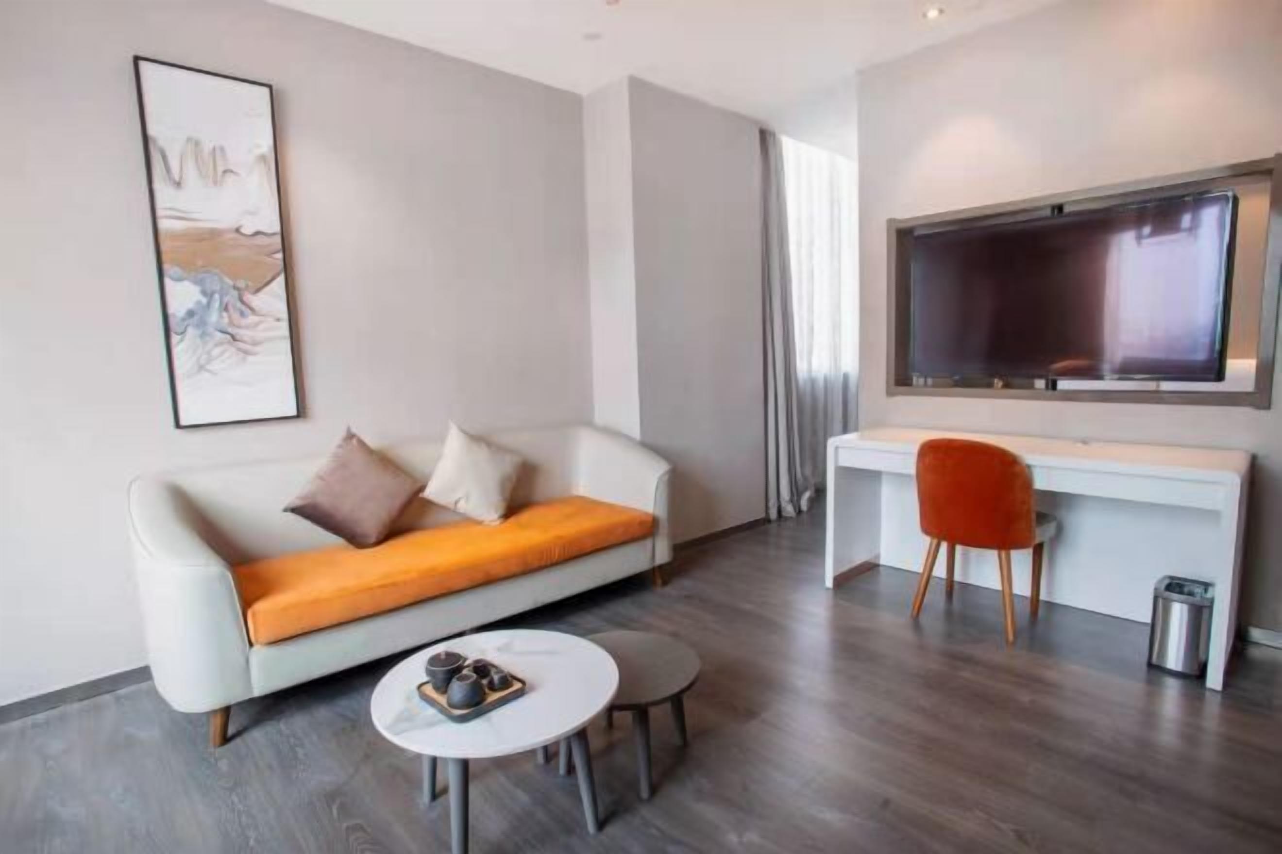 Ein modernes Wohnzimmer mit einer Couch, einem kleinen runden Tisch, einem Schreibtisch mit Stuhl und einem großen Fernseher.