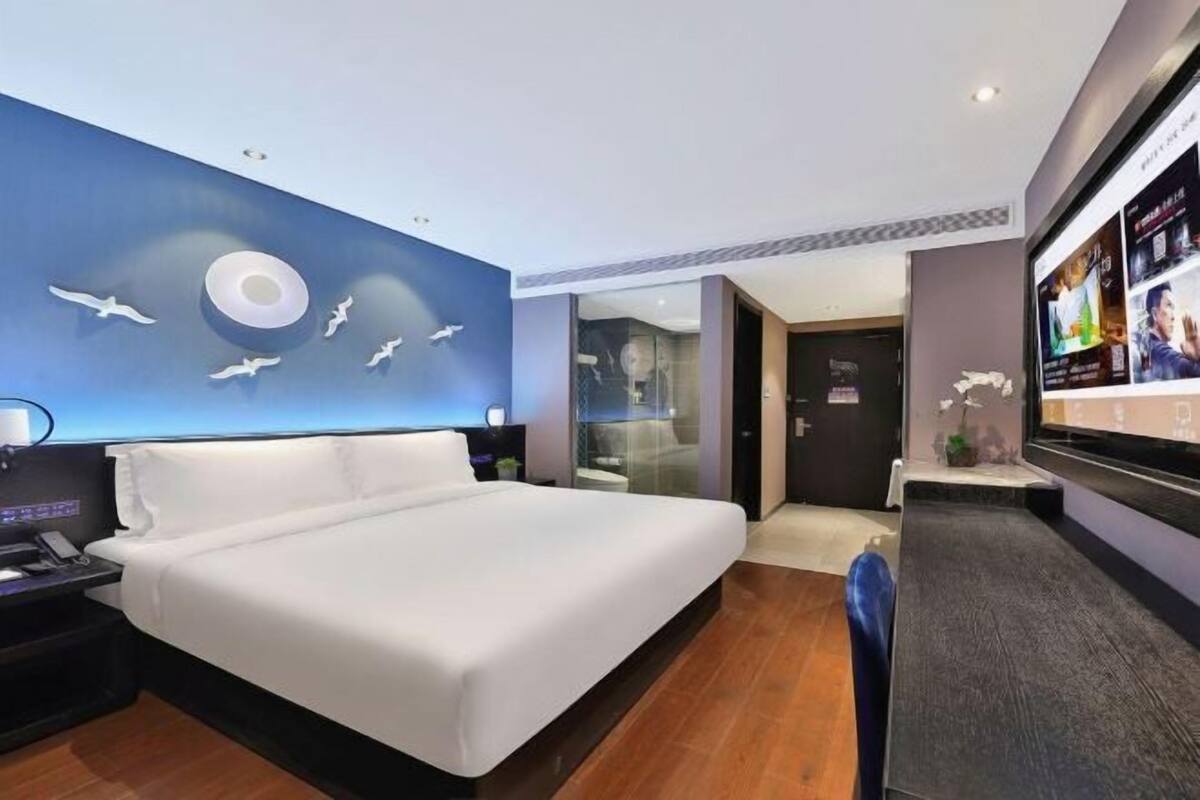 A hotel room with a large bed, a TV, a desk with a lamp, and a wall with a circular design and flying birds.