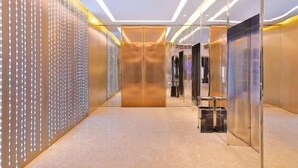A modern elevator with a metallic finish and a glass door, surrounded by a wall with hanging lights and a textured panel. - Crystal Orange Xu Zhou Su Ning Guang Chang (Xuzhou)