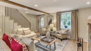 Un salon spacieux avec un escalier, une table basse et une vue sur l’extérieur grâce à de grandes fenêtres.