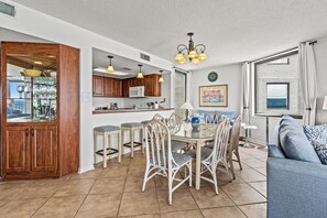 A spacious living area with a dining table, chairs, and a sofa. There is a kitchen area with wooden cabinets and a microwave.