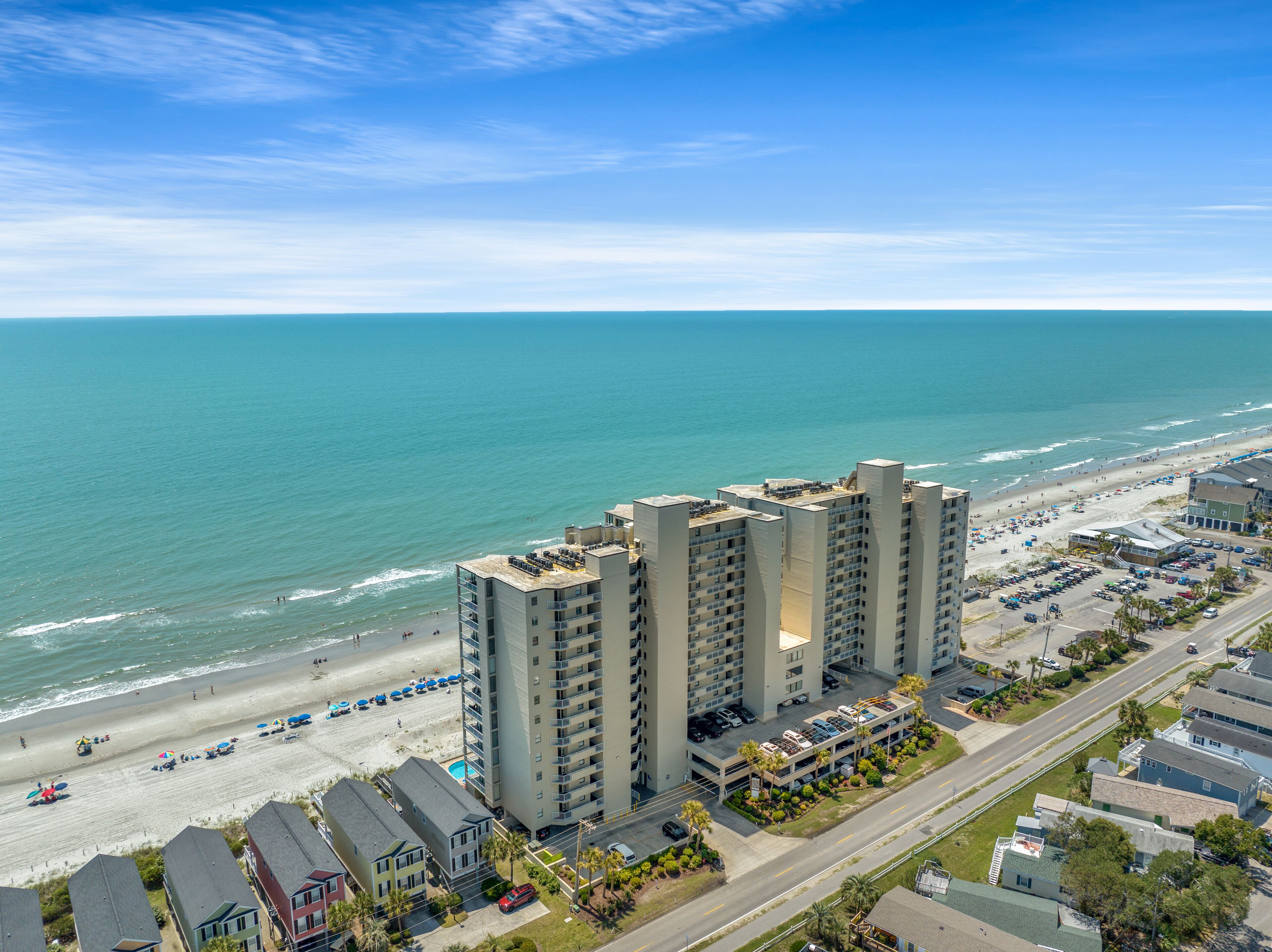 A high-rise hotel with a beach view, parking, and a road.
