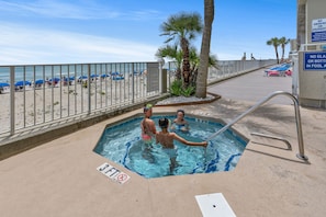 A swimming pool with a metal ladder, a beach with umbrellas, and a palm tree.