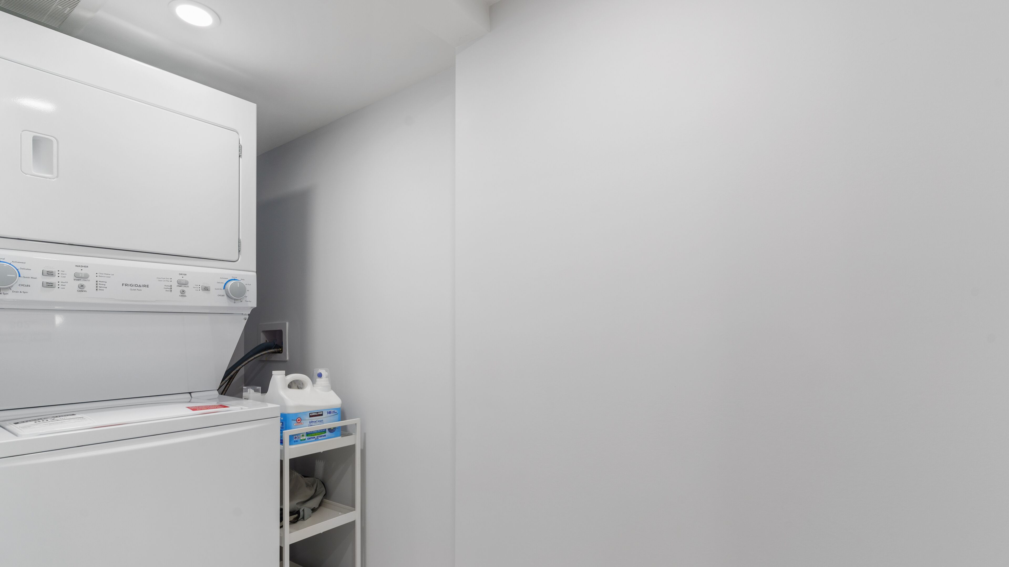 A laundry area with a front-loading washing machine and a dryer. There is a shelf with detergent bottles and a box of detergent.